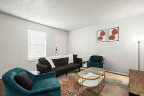 Ein Wohnzimmer mit einer Couch, zwei Sesseln, einem Glastisch und einer Stehlampe.