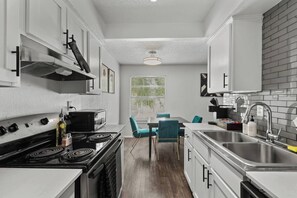 Cozinha compacta com fogão, micro-ondas e pia. Possui área de refeições com cadeiras e mesa.