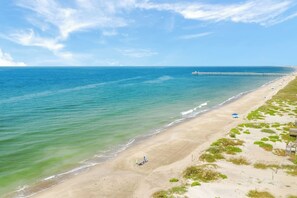 A beach with a pier extending into the ocean, clear skies, and a sandy shoreline. - Biển Kay – Luxury Beach House w/ Pool + Golf Cart (Holden Beach)