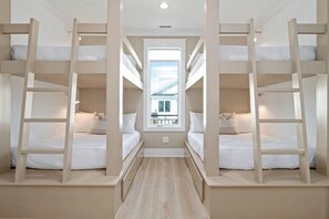 A room with bunk beds, a window, and a view of a building outside. - Biển Kay – Luxury Beach House w/ Pool + Golf Cart (Holden Beach)