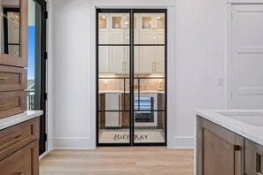 A modern kitchen with wooden cabinets, a white countertop, and a glass door with the text 'BIÈNKAY'. - Biển Kay – Luxury Beach House w/ Pool + Golf Cart (Holden Beach)
