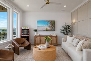 A living room with a sofa, armchair, coffee table, and a television. - Biển Kay – Luxury Beach House w/ Pool + Golf Cart (Holden Beach)