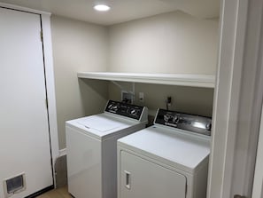 A laundry room with two front-loading washing machines and a dryer, a white door, and a shelf above the machines.
