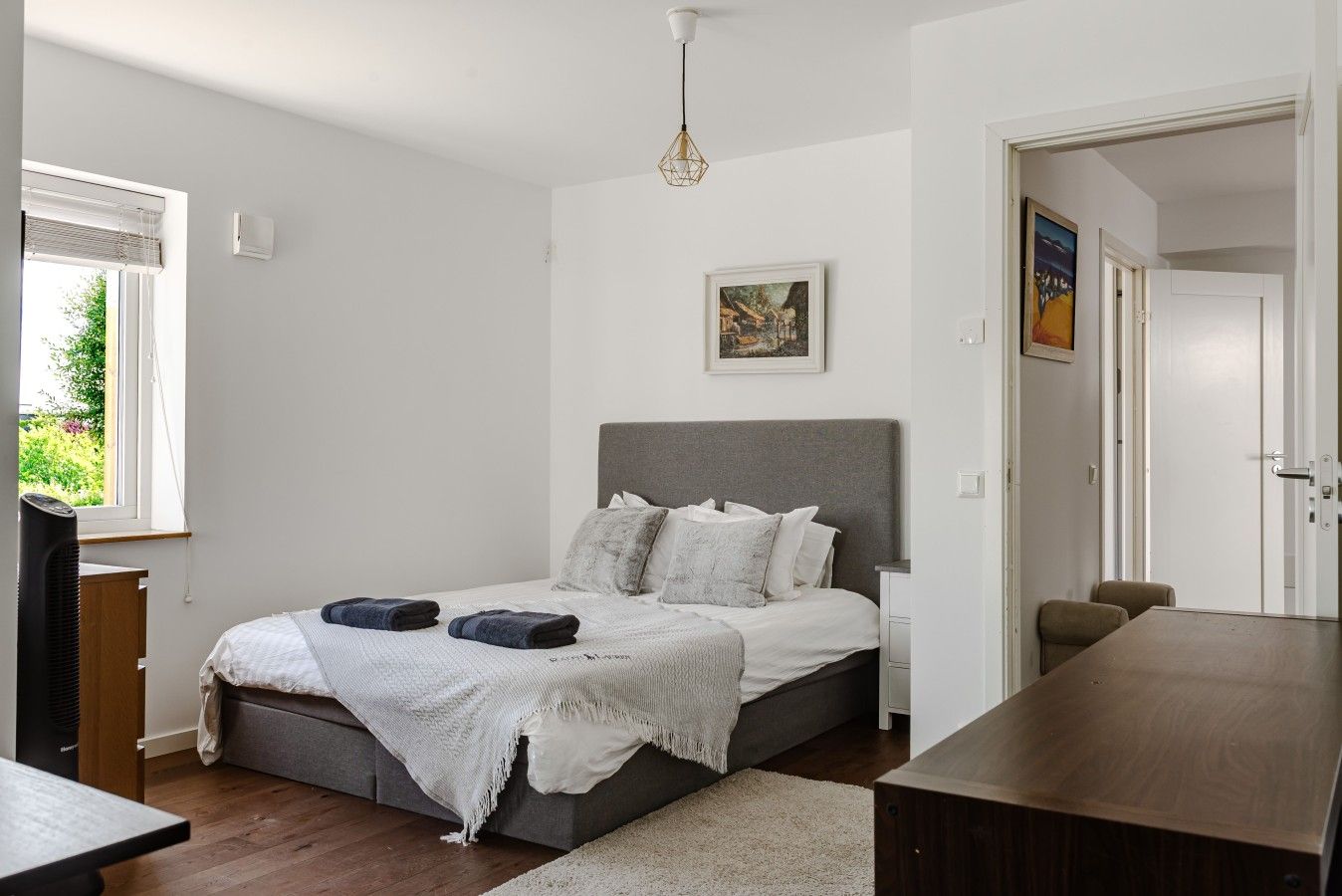 Ein Schlafzimmer mit einem Bett, Nachttischen, einem Schreibtisch und einem Fenster mit Jalousien.
