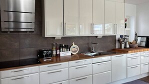 Uma cozinha moderna com armários brancos, exaustor de aço inoxidável e bancada de madeira.