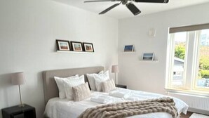 Quarto com cama, ventoinha no teto, mesa de cabeceira e janela com luz natural.