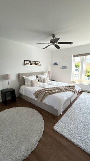 Ein Schlafzimmer mit Bett, Deckenventilator, Nachttisch und einem Fenster mit Tageslicht.