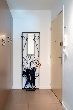 A hallway with a metal rack holding umbrellas, a door with a light switch, and a wall-mounted telephone. - Le Palm Beach aperçu mer avec balcon proche plages (Cannes)