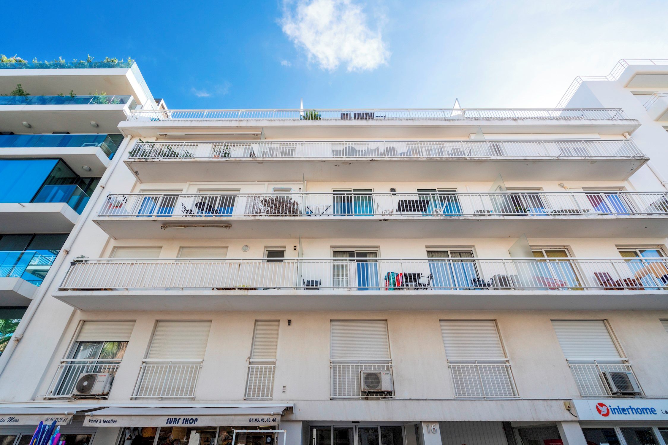 A multi-story building with balconies, air conditioning units, and a surf shop on the ground floor.