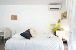 Ein Hotelzimmer mit Bett, Schreibtisch, Stuhl, Klimaanlage, Pflanze und Lampe.