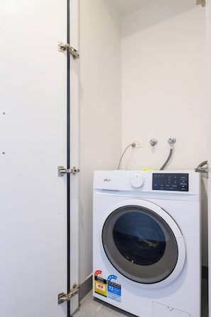 A compact, white, wall-mounted washing machine with a control panel and a water rating label. - Banque Nook Cosy Southbank Stay near Crown and Yarra (Southbank)