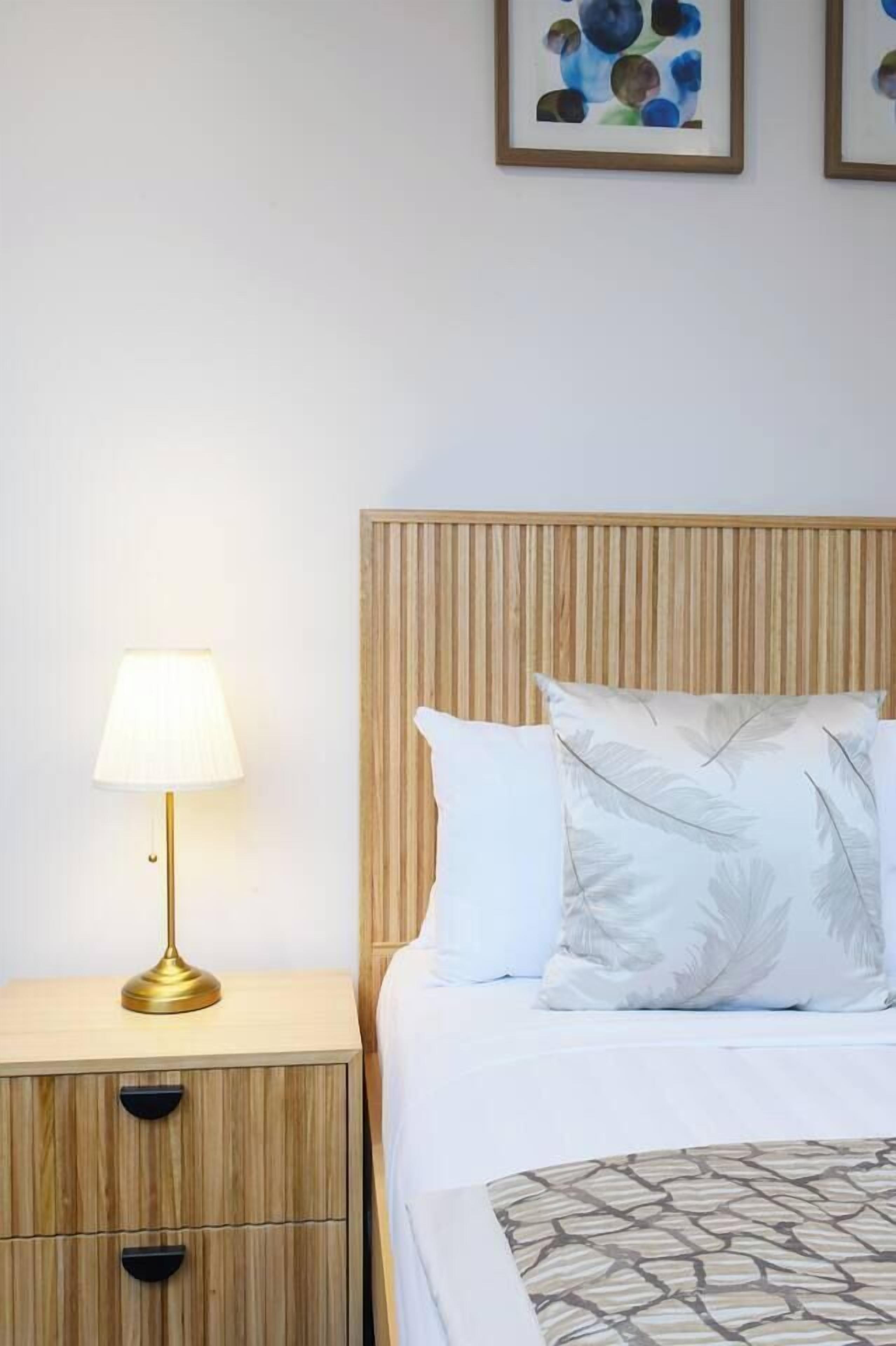 A neatly made bed with a wooden headboard, a bedside lamp, and a nightstand with drawers.