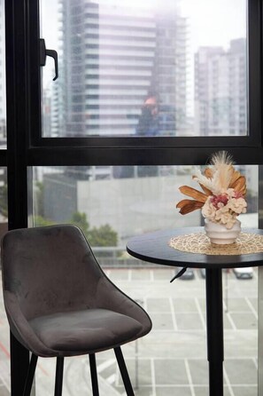 A modern room with a view of a cityscape through a large window, a round table with a vase of flowers, and a single chair. - Protea Corner Laid back CBD Stay by Yarra and Dining (Southbank)