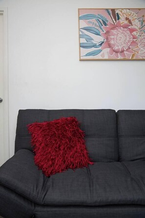 A grey sofa with a red textured pillow against a white wall, and a floral painting above it. - Protea Corner Laid back CBD Stay by Yarra and Dining (Southbank)