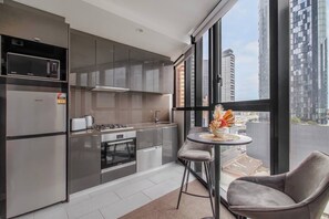 A modern kitchen with stainless steel appliances, a dining area with a table and chairs, and a large window offering a city view. - Protea Corner Laid back CBD Stay by Yarra and Dining (Southbank)