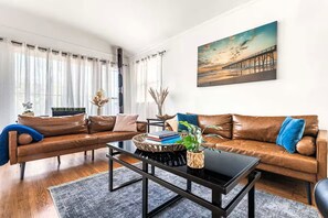 Ein Wohnzimmer mit einem braunen Ledersofa, einem schwarzen Couchtisch und einem Gemälde eines Piers an der Wand.