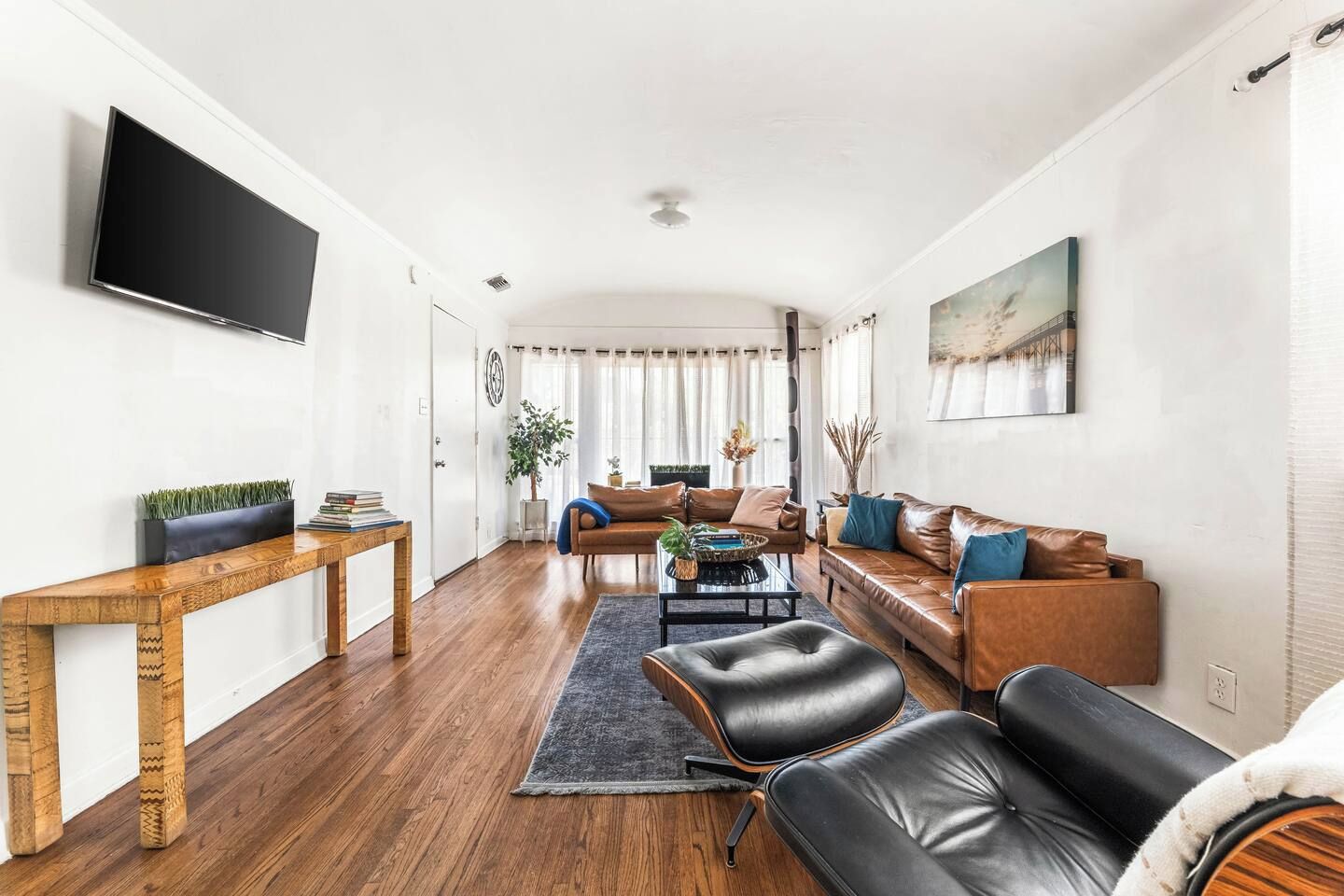 Una sala de estar moderna con una mesa de centro de madera, sofás de cuero, un televisor de pantalla plana y un ventanal con cortinas.