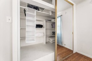 Ein begehbarer Kleiderschrank mit offenen Regalen, einer Kleiderstange und einem Duschbereich mit blauer Duschvorhang.