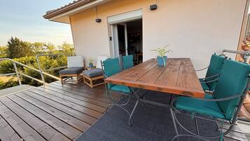 Una terraza de madera con una mesa y sillas, una planta en maceta y una puerta que da a un espacio interior.