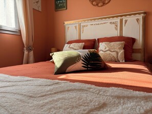 A bed with a white textured cover, a green and white pillow, and multiple red pillows.
