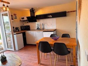 A compact kitchen with white appliances, a wooden dining table, and black chairs.