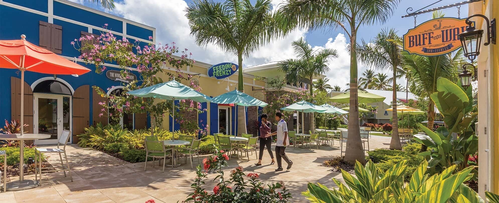 An outdoor patio area with tables and chairs, surrounded by lush greenery and palm trees.