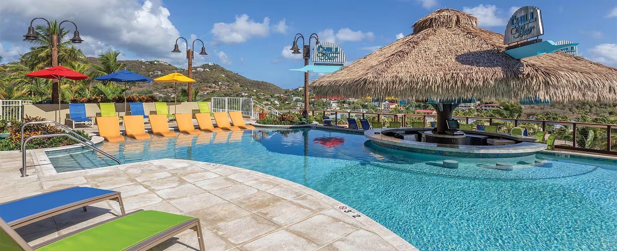 A pool area with lounge chairs, umbrellas, and a thatched roof structure.