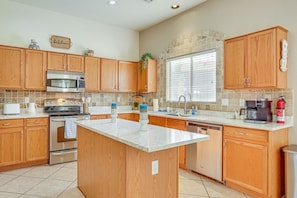 A kitchen with wooden cabinets, a central island, stainless steel appliances, and a stone backsplash. - The Surprise Oasis, Heated Pool, Pet Friendly (Surprise)