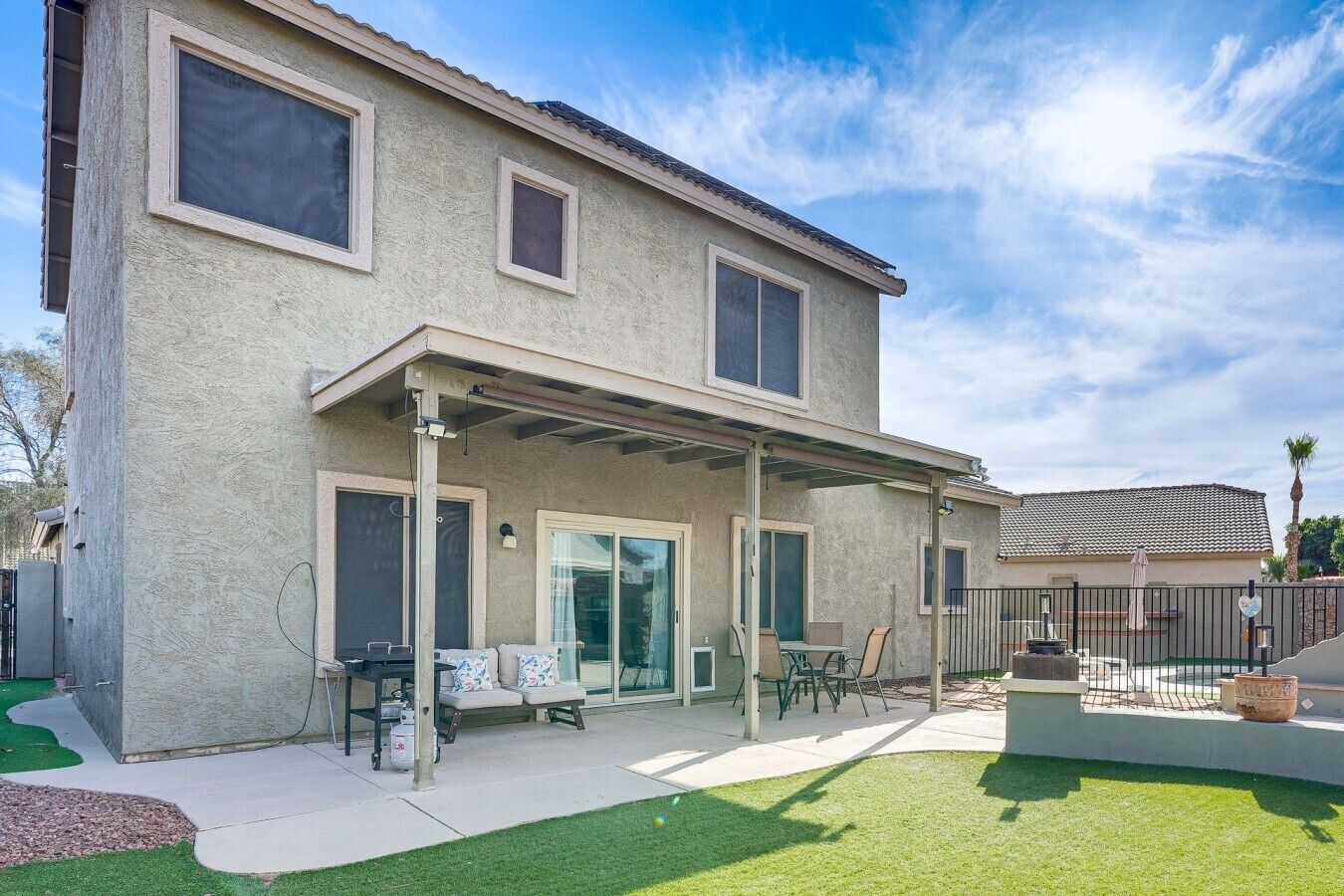 A two-story house with a covered patio, a lawn, and a fenced backyard.