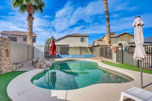 A swimming pool with a stone wall, palm trees, and a red umbrella. - The Surprise Oasis, Heated Pool, Pet Friendly (Surprise)