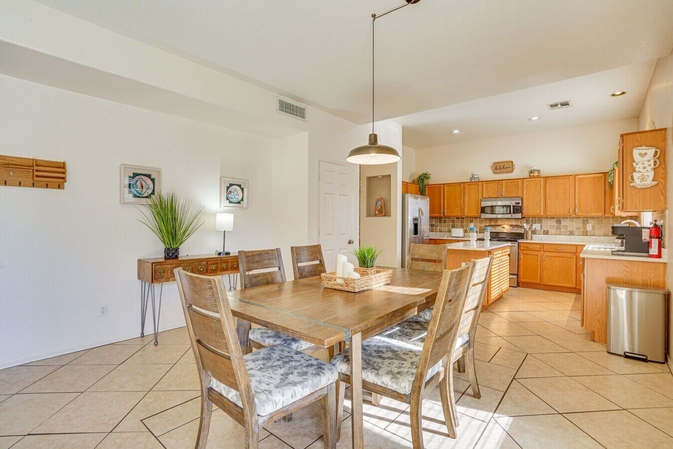 A modern kitchen with wooden cabinets, a stainless steel refrigerator, and a dining area with a wooden table and chairs.