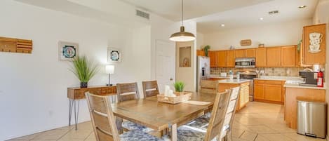 A modern kitchen with wooden cabinets, a stainless steel refrigerator, and a dining area with a wooden table and chairs.