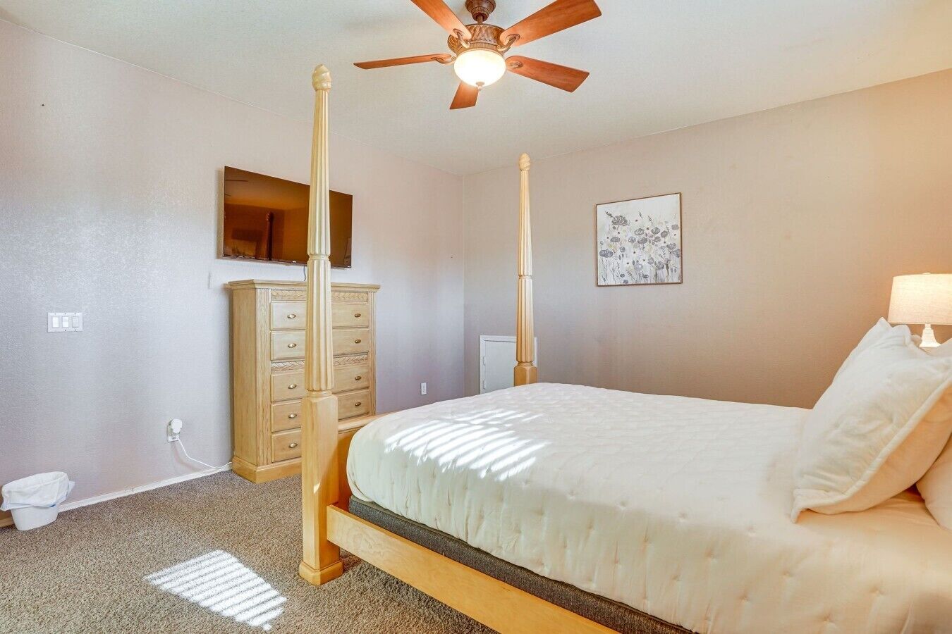 A bedroom with a four-poster bed, a ceiling fan, a dresser, and a wall-mounted TV.