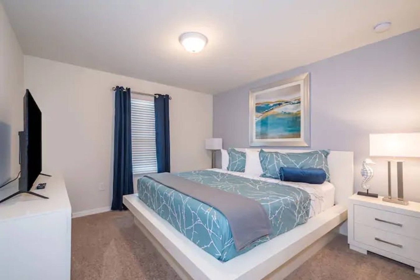 A bedroom with a bed, a television, a nightstand, and a painting on the wall.