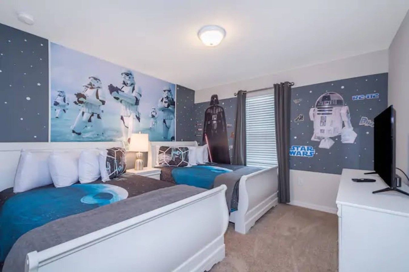 Una habitación con dos camas, un escritorio, un televisor y decoración de pared temática de Star Wars.