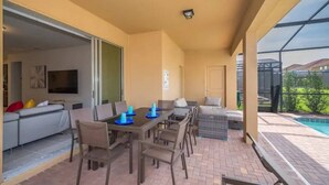 An outdoor patio with a dining table and chairs, a sofa, and a pool. - 7BR Solterra Resort Themed Home, Games, Fun,Disney (Davenport)