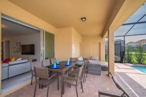 An outdoor patio with a dining table and chairs, a sofa, and a pool. - 7BR Solterra Resort Themed Home, Games, Fun,Disney (Davenport)