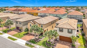 A residential area with multiple houses featuring red-tiled roofs, well-maintained lawns, and palm trees. - 7BR Solterra Resort Themed Home, Games, Fun,Disney (Davenport)
