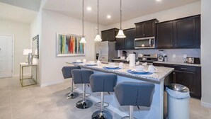 A modern kitchen with dark cabinets, a central island with bar stools, and pendant lighting. - 7BR Solterra Resort Themed Home, Games, Fun,Disney (Davenport)