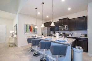A modern kitchen with dark cabinets, a central island with bar stools, and pendant lighting. - 7BR Solterra Resort Themed Home, Games, Fun,Disney (Davenport)
