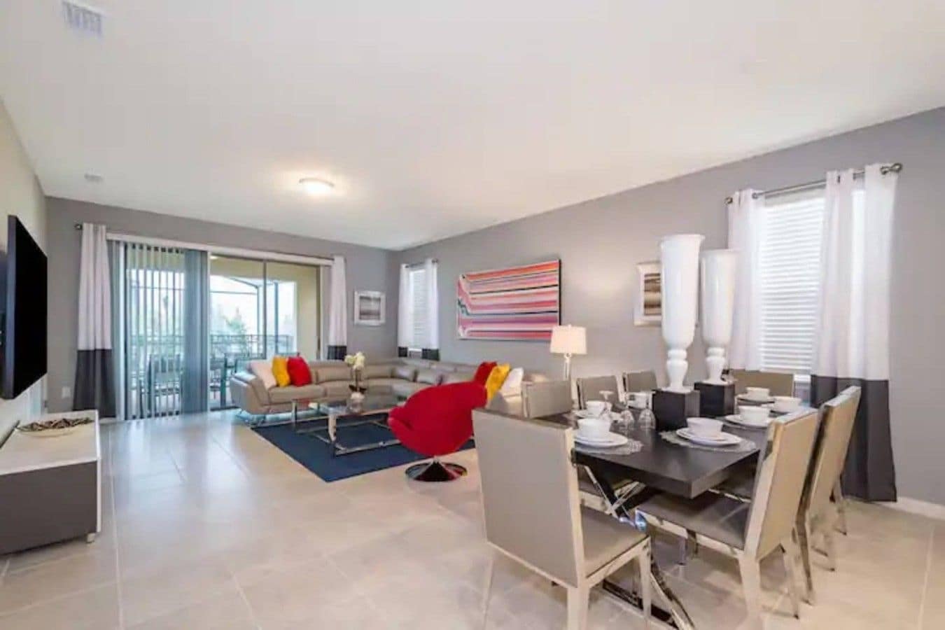 A modern living room with a sofa, a red chair, and a dining area with a table set for four.