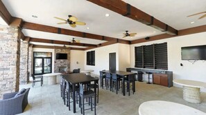 An outdoor patio area with a stone fireplace, multiple dining tables, chairs, and ceiling fans. - 7BR Solterra Resort Themed Home, Games, Fun,Disney (Davenport)