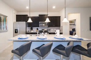 A modern kitchen with dark cabinets, a central island with bar stools, and pendant lighting. - 7BR Solterra Resort Themed Home, Games, Fun,Disney (Davenport)