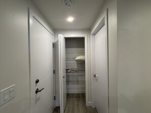 A narrow hallway with white doors leading to a closet with shelves and folded blankets. - Paradise in Glenridding (Edmonton)