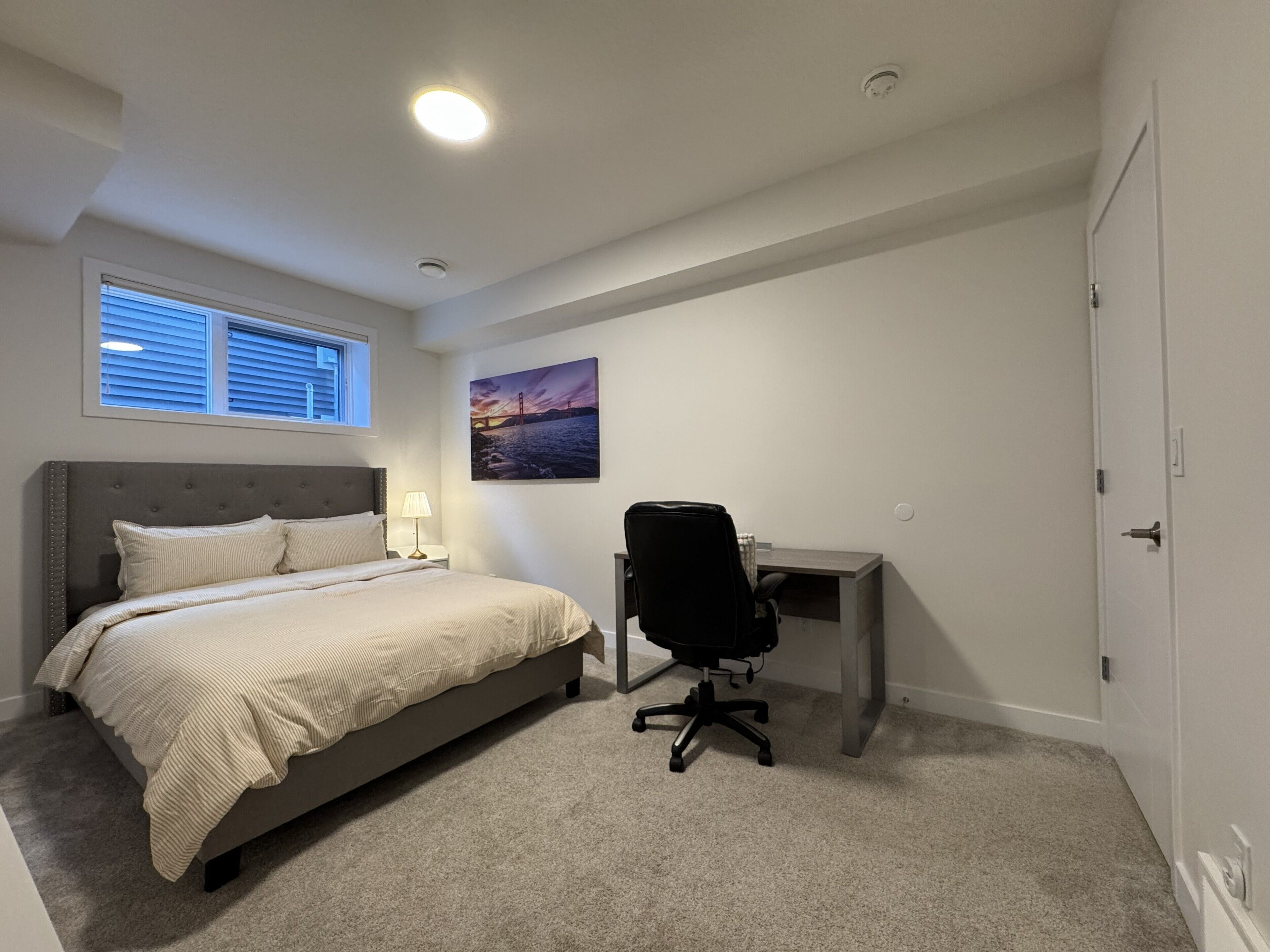 Ein Schlafzimmer mit einem Bett, einem Schreibtisch, einem Stuhl, einem Fenster und einem Bild an der Wand.