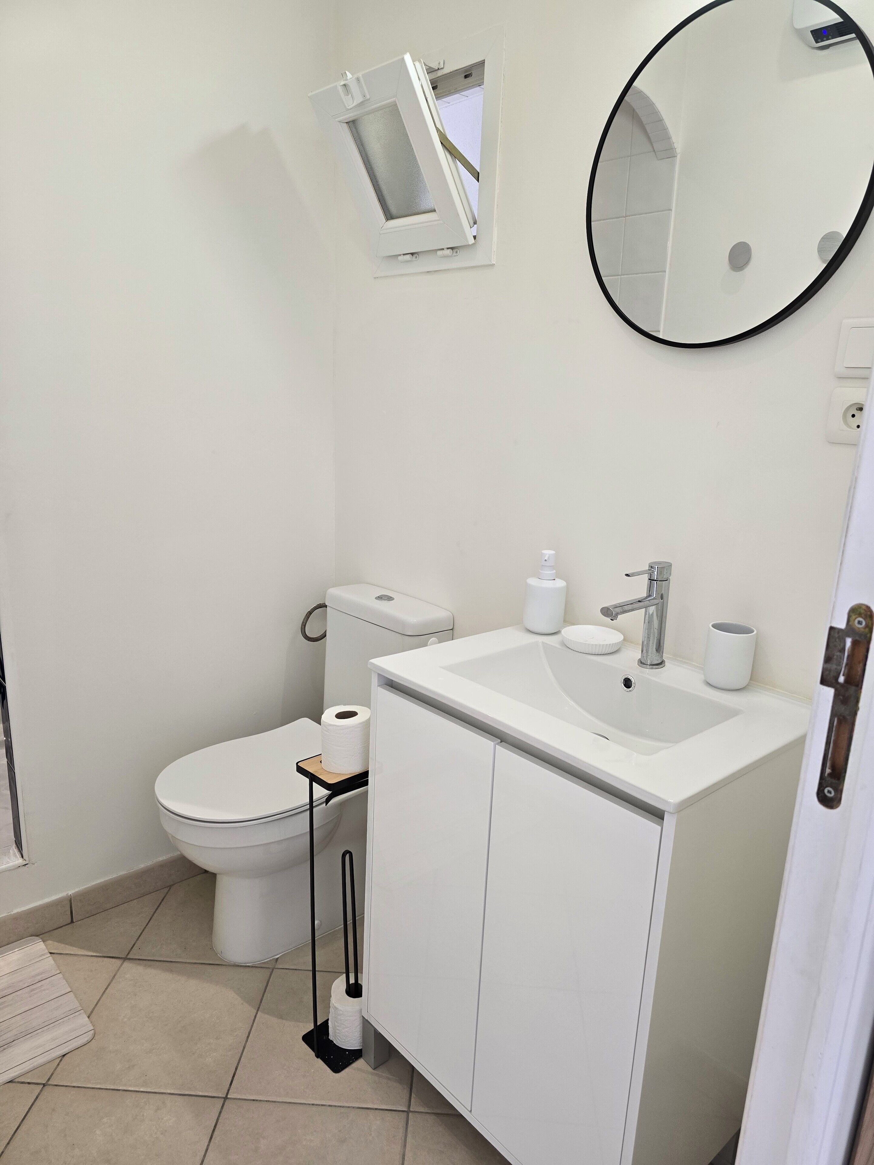Une salle de bain avec des toilettes, un lavabo, un miroir et une petite fenêtre.