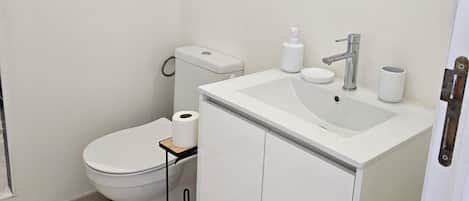 A bathroom with a toilet, sink, mirror, and a small window.