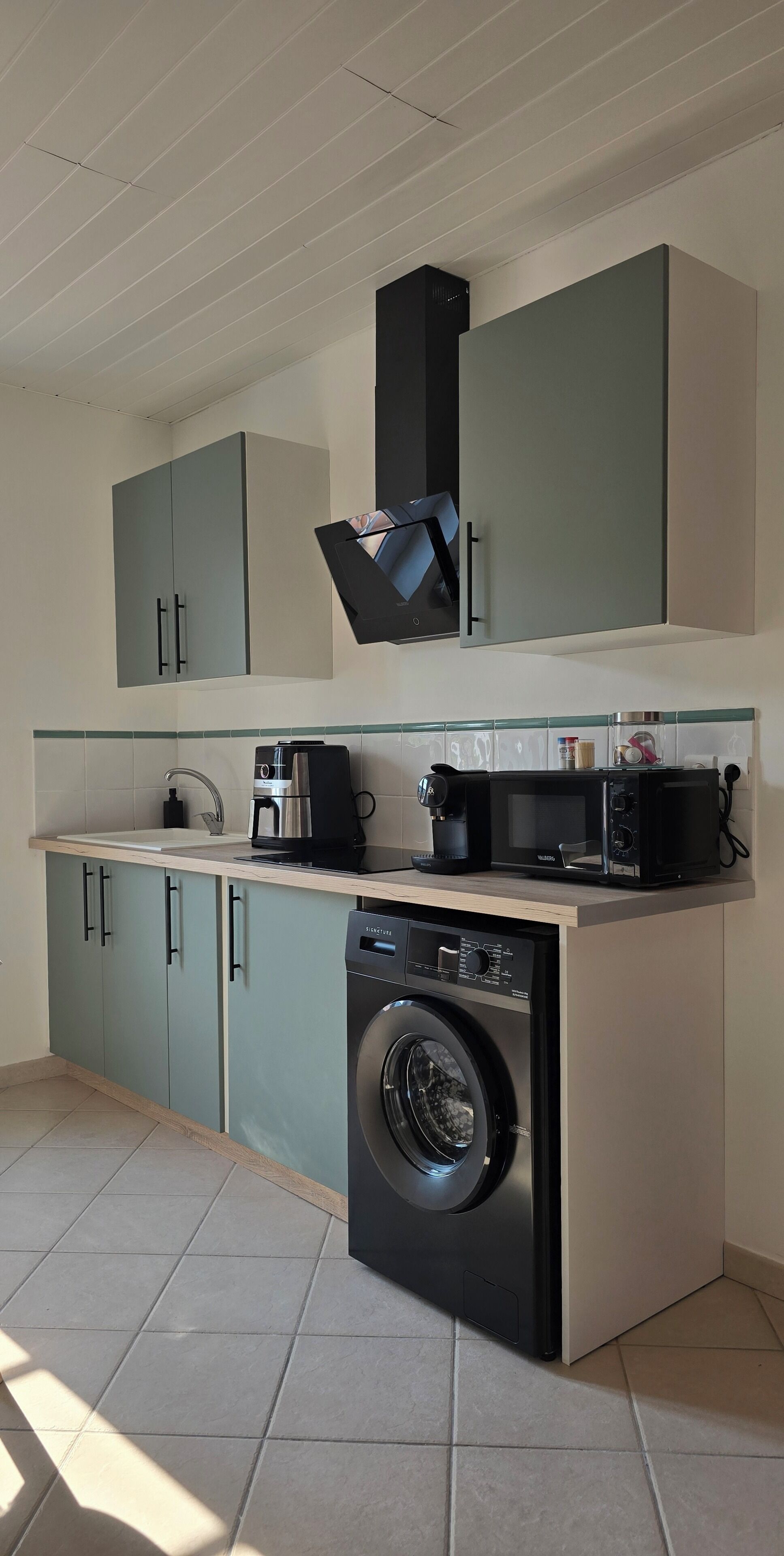 A compact kitchen with a built-in washing machine, a coffee maker, and a microwave.