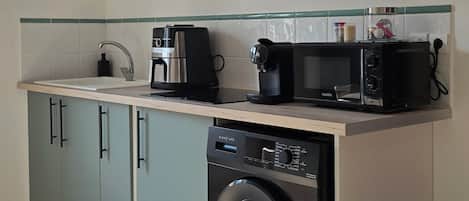 A compact kitchen with a built-in washing machine, a coffee maker, and a microwave.