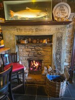 Una chimenea con un pez montado encima, un letrero que dice 'The Rusty Mackerel 1892' y una pared de piedra.